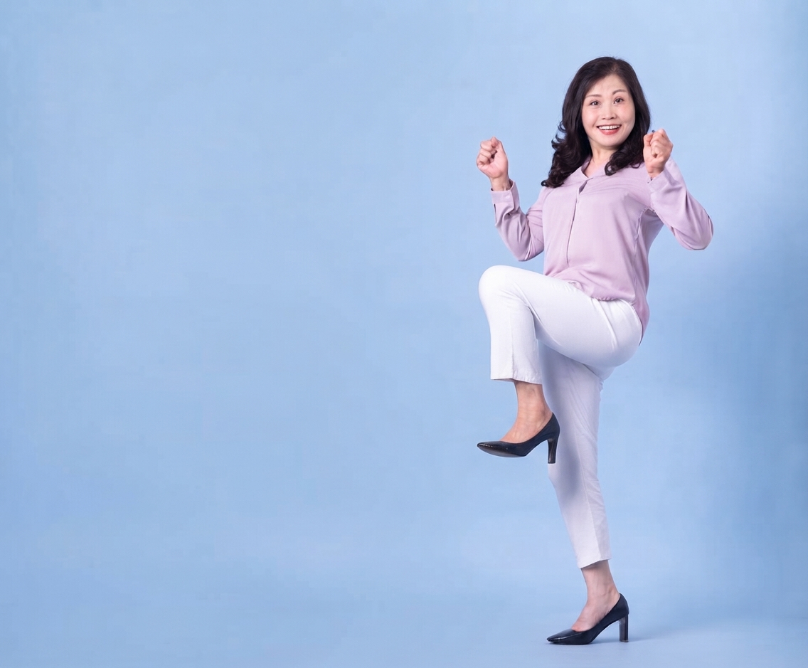 Smiling woman standing and laughing, mid-step, in front of a plain blue wall